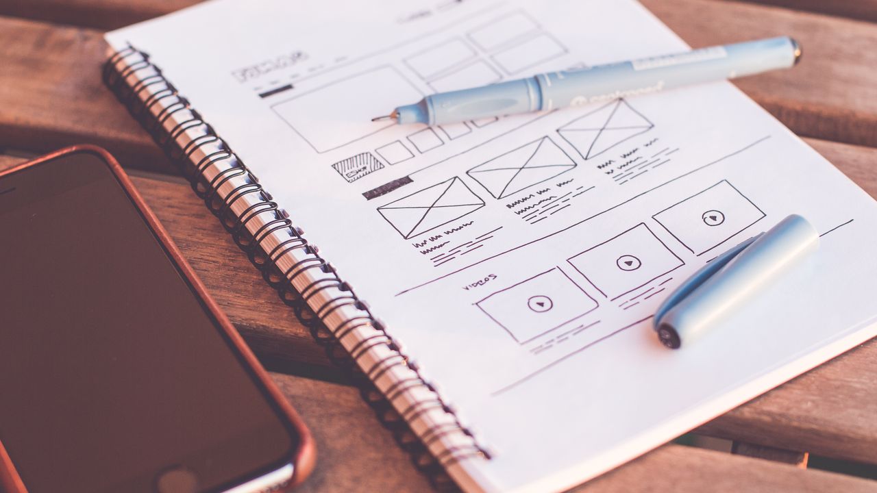 A mobile app wireframe sketched on a notepad beside a smartphone