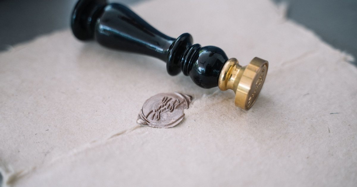 A brass wax-seal stamp resting beside a fresh seal on handmade paper