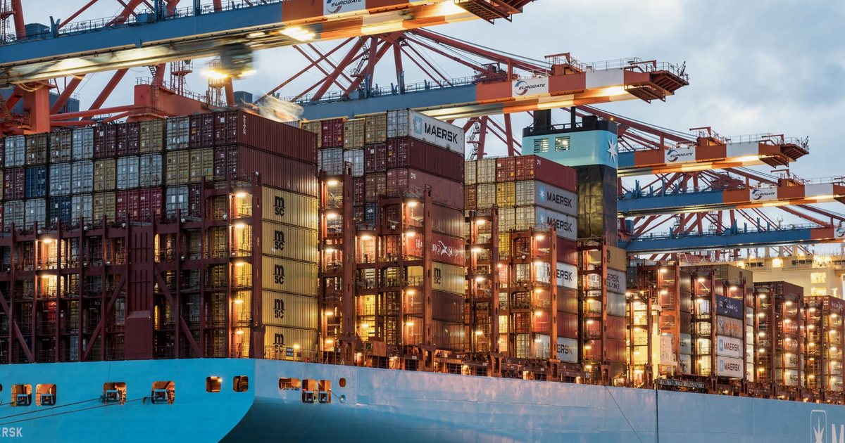 A container ship stacked with shipping containers under port cranes at dusk